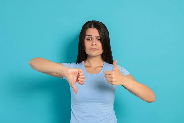 Young woman showing thumbs up and down on light blue background