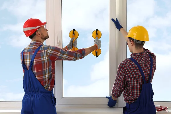 Workers using suction lifters during plastic window installation indoors