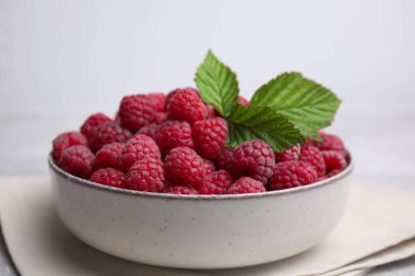 Bowl of fresh ripe raspberries with green leaves on table, closeup