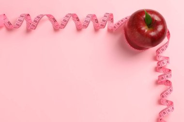 Fresh red apple with measuring tape on pink background, flat lay. Space for text