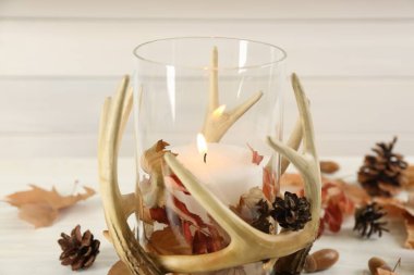 Stylish holder with burning candle and autumn decor on white wooden table, closeup