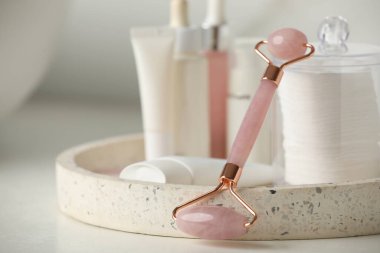 Natural face roller and tray with cosmetic products on white table, closeup
