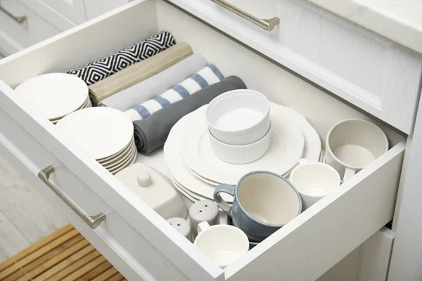 Open drawer of kitchen cabinet with different dishware and towels