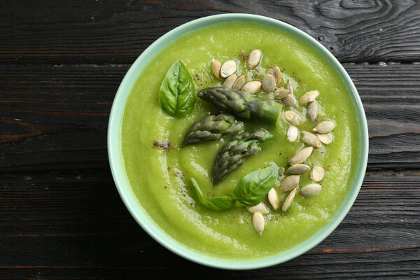 Delicious asparagus soup in bowl on black wooden table, top view