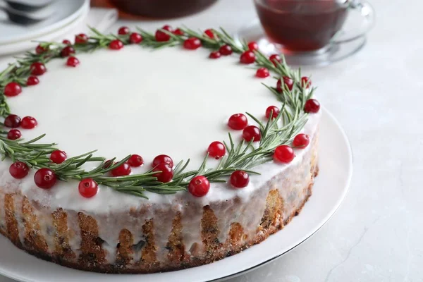 Traditional Christmas cake decorated with rosemary and cranberries on light table, closeup
