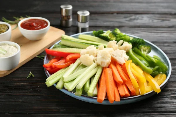 Plate with celery sticks, other vegetables and different dip sauces on dark wooden table