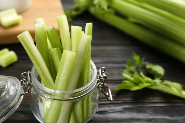 Celery sticks in jar on dark wooden table, closeup. Space for text