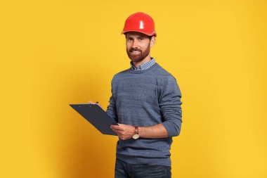 Professional engineer in hard hat with clipboard on yellow background