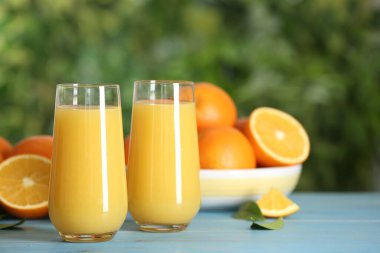 Delicious orange juice on light blue wooden table against blurred background. Space for text