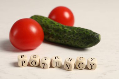 Cubes with word Potency near cucumber and tomatoes symbolizing male genitals on white wooden table