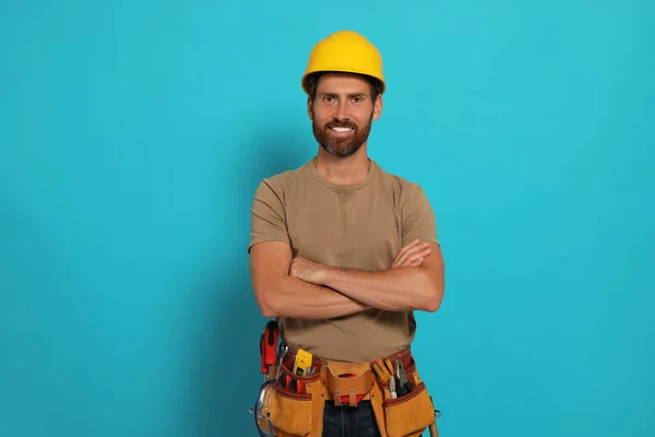Professional builder in hard hat with tool belt on light blue background
