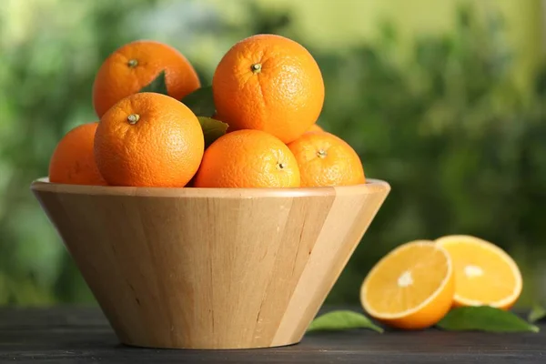 Fresh ripe oranges in bowl on wooden table against blurred background