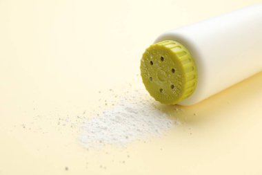 Bottle and scattered dusting powder on beige background, closeup. Baby cosmetic product
