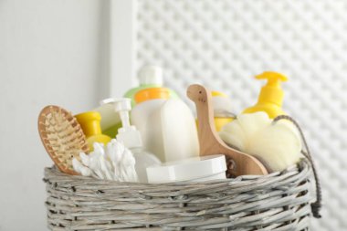 Wicker basket full of different baby cosmetic products, accessories and toy on blurred background, closeup