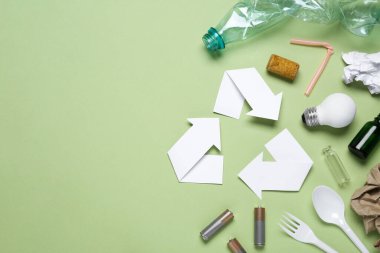 Recycling symbol and garbage on light green background, flat lay. Space for text