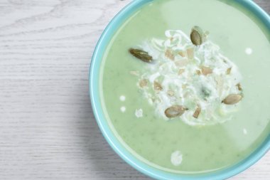 Bowl of delicious asparagus soup on white wooden table, top view. Space for text