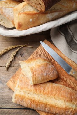 Different tasty baguettes, knife and spikelets on wooden table, flat lay