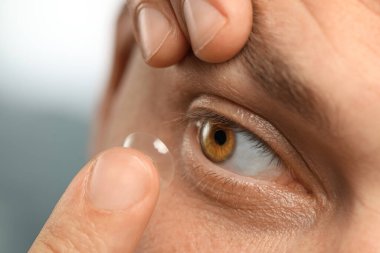 Man putting contact lens in his eye on blurred background, closeup