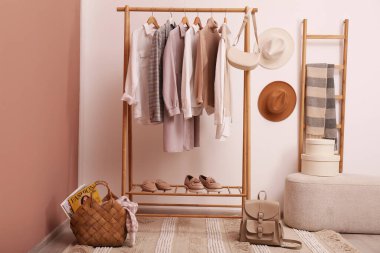 Odada beyaz duvarın yanında farklı şık kıyafetler ve ayakkabılar var.