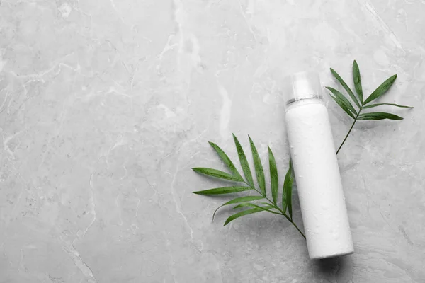 Dry shampoo spray and green leaves on light grey table, flat lay. Space for text