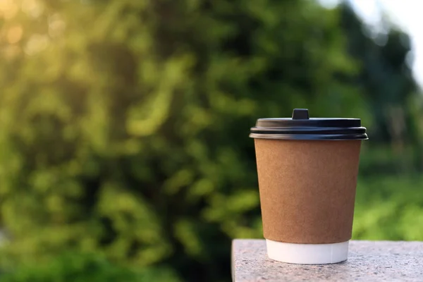 Disposable paper cup with plastic lid on stone parapet outdoors, space for text