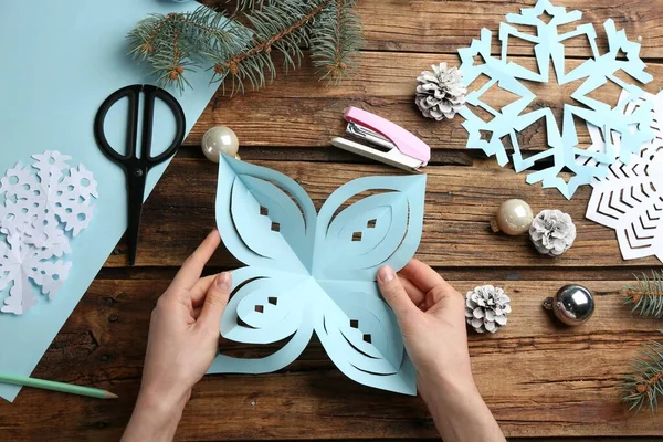 Woman making paper snowflake at wooden table, top view