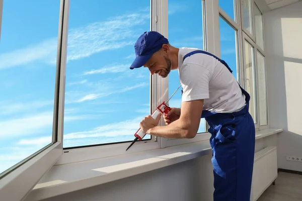 Worker sealing plastic window with caulk indoors. Installation process