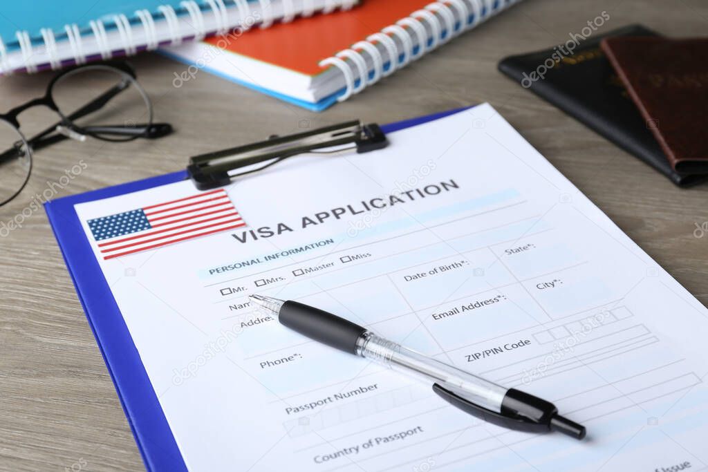 Visa application form for immigration to USA and pen on wooden table, closeup