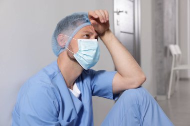 Hastane koridorundaki gri duvarın yanında yorgun bir doktor var.