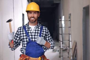 Professional builder in uniform with hammer and tool belt indoors