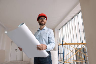 Professional engineer in hard hat with draft indoors, low angle view