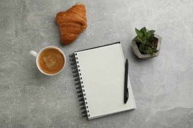 Not defteri, bir fincan aromatik kahve, lezzetli kruvasan ve gri masanın üzerine serilmiş bitki.