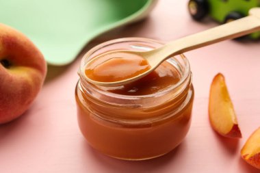 Cam kavanozun üzerinde sağlıklı bebek mamasıyla pembe ahşap masada, yakın plan.