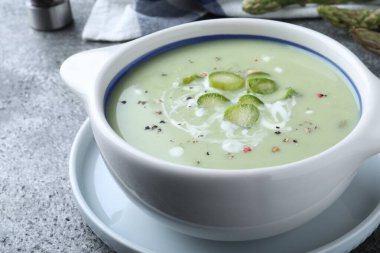 Bowl of delicious asparagus soup on grey table, closeup