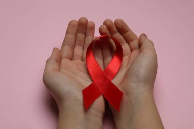 Pembe arka planda kırmızı kurdele tutan küçük kız, yakın plan. AIDS Hastalığı Farkındalığı