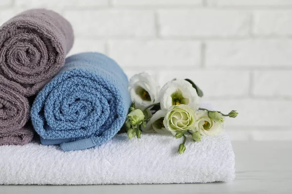 Rolled and folded towels with flowers on white table, closeup. Space for text