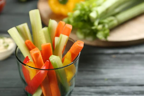 Celery and other vegetable sticks in glass on grey wooden table, closeup. Space for text