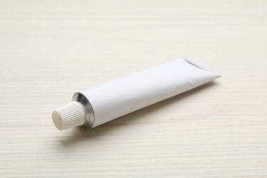 Blank white tube of ointment on light wooden table. Space for text