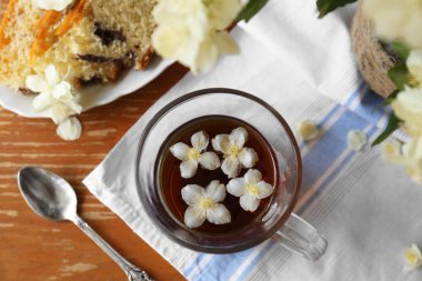 Glass cup of aromatic tea with beautiful jasmine flowers and dessert on wooden table, flat lay