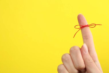 Sarı arka planda bağlı kırmızı fiyonklu işaret parmağı gösteren kadın, yakın plan. Metin için boşluk