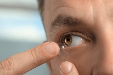 Man putting contact lens in his eye on blurred background, closeup