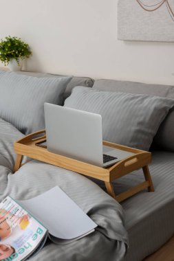 Wooden tray table with laptop and smartphone on bed indoors