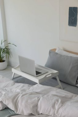 White tray table with laptop on bed indoors