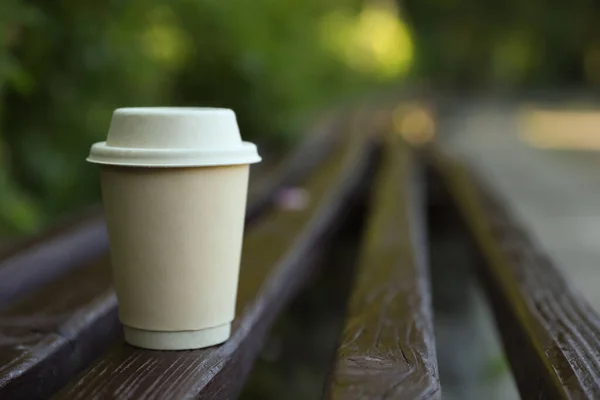 Cardboard takeaway coffee cup with lid on wooden bench outdoors, space for text