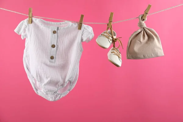 Baby clothes hanging on washing line against pink background