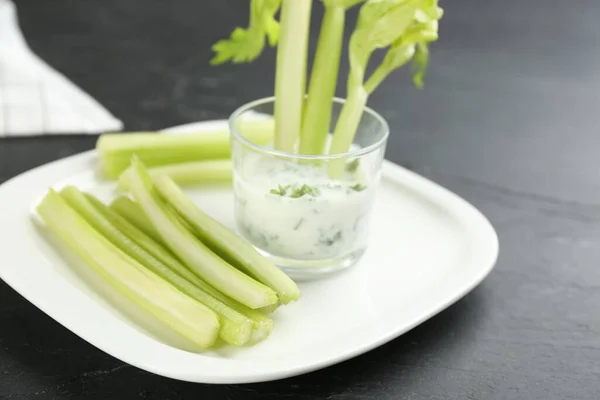 Celery sticks with dip sauce in glass on black table, closeup