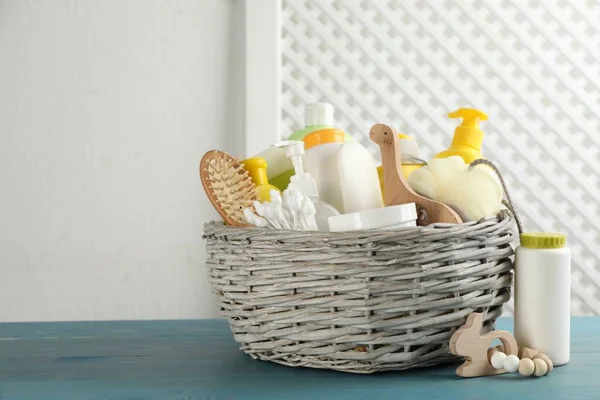 Wicker basket with different baby cosmetic products, accessories and toys on light blue wooden table. Space for text