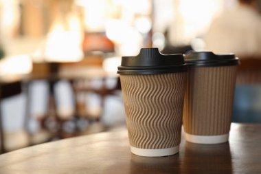 Cardboard takeaway coffee cups with plastic lids on wooden table in city, space for text