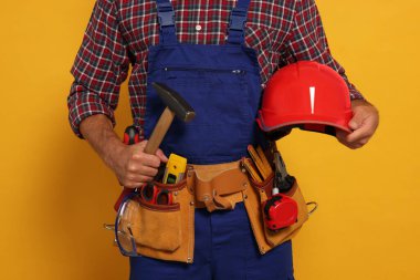 Professional builder in uniform with hammer and tool belt on yellow background, closeup