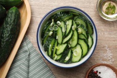 Delicious salad with cucumbers and green onion in bowl on wooden table, flat lay
